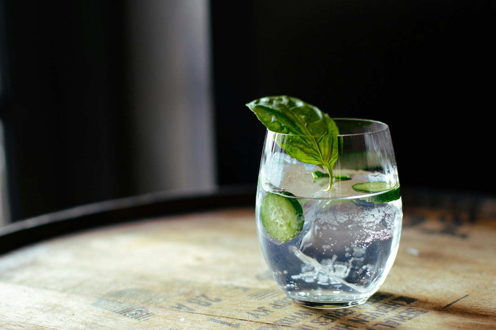 Copo de gin tônica com gelo e rodela de limão sobre balcão de madeira ao entardecer