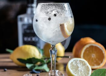 Garrafa de gin London Dry sobre mesa de madeira ao lado de embalagem de presente e taça vazia