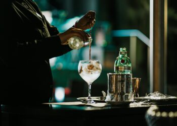 Copo alto de gin tônica com gelo abundante e casca de limão siciliano sobre bancada de mármore
