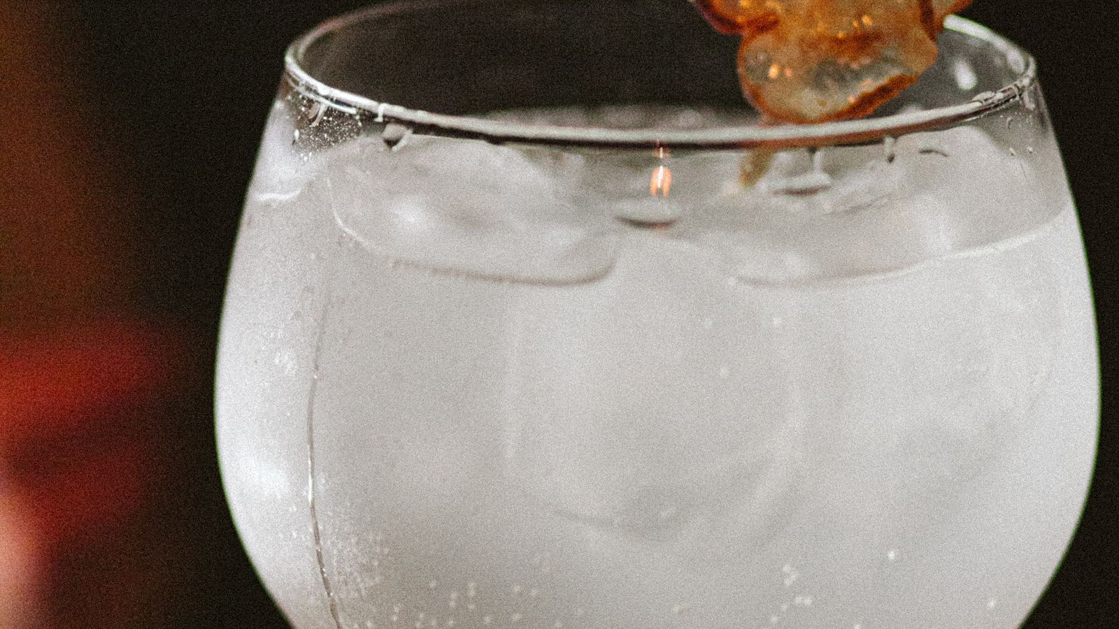 Taça de drink com gin e frutas vermelhas sobre balcão claro com gelo e casca de limão