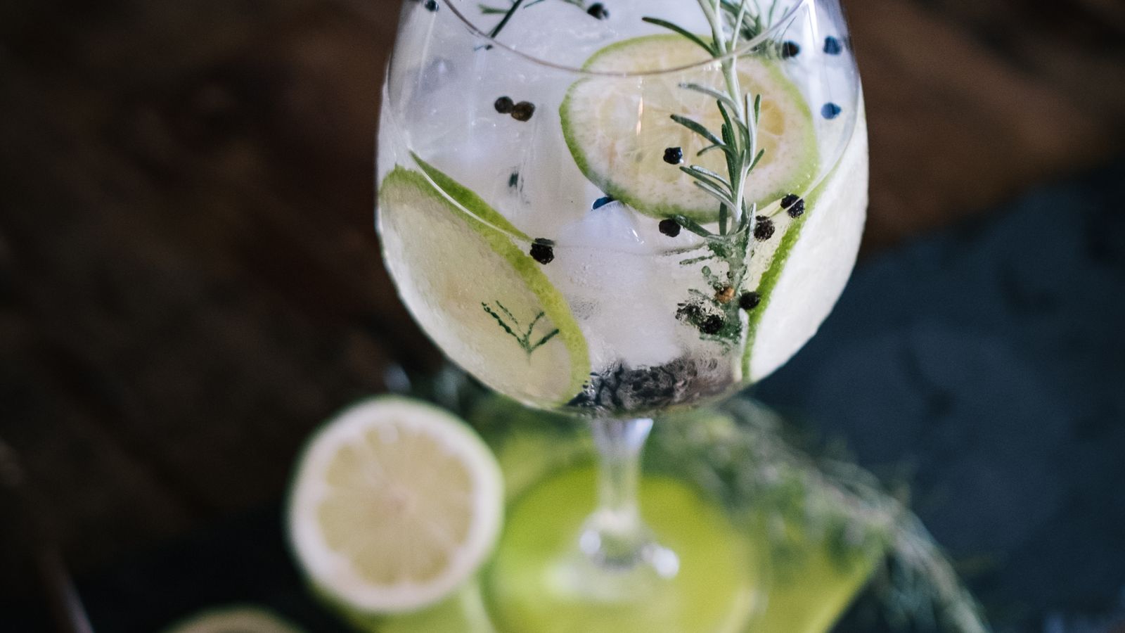 Taça de gin tônica com gelo abundante e casca de limão sobre balcão claro